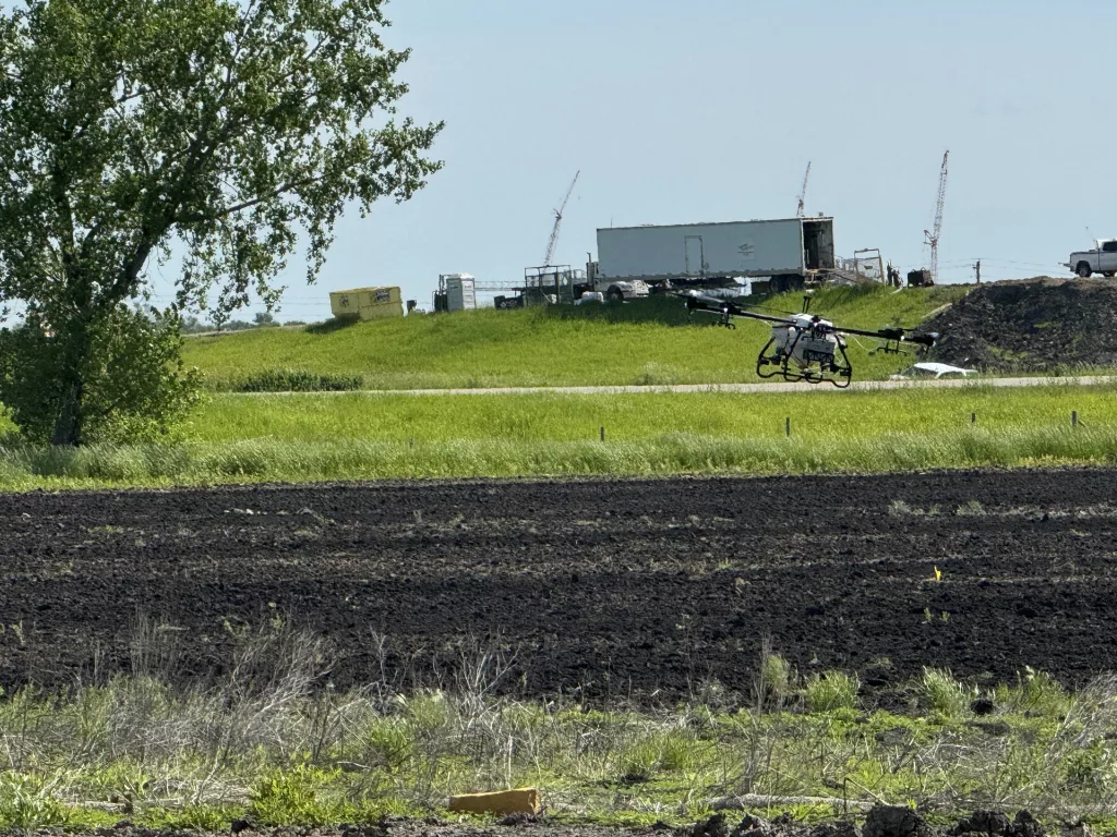 A done fitted with sprayers flying across a field.