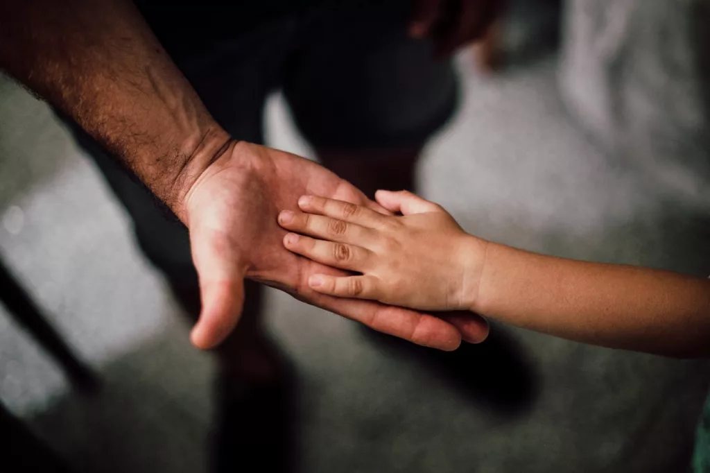 Photo of dad touching child's hand.