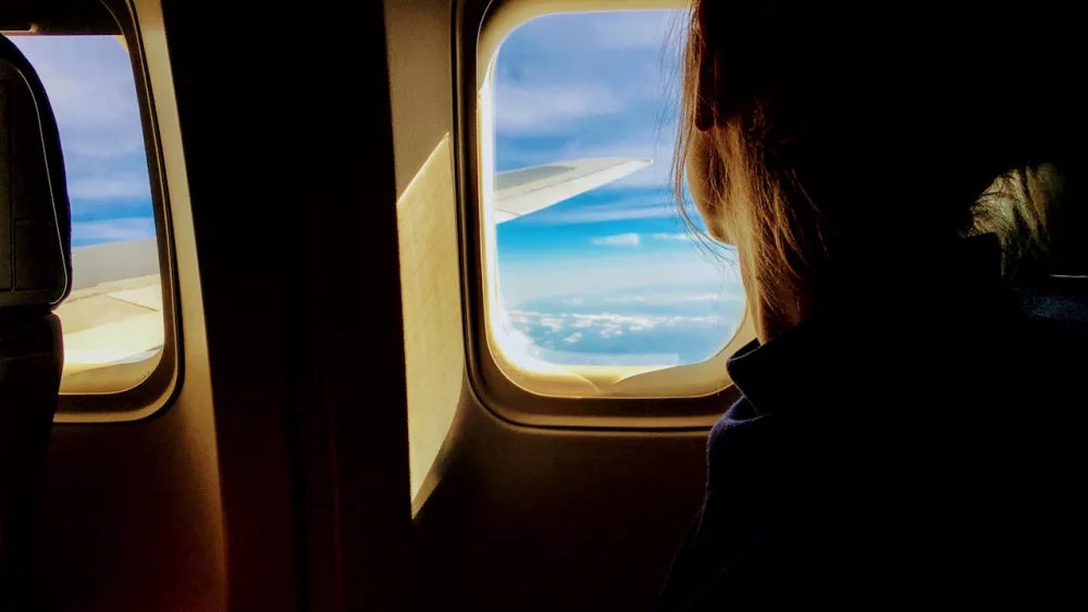 Photo shows passenger looking out plane window.