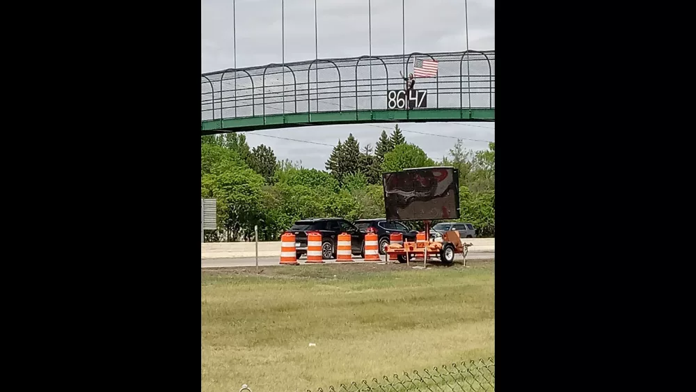 Image of Judd Hoff displaying an "8647" banner on Fargo's I-94 pedestrian bridge