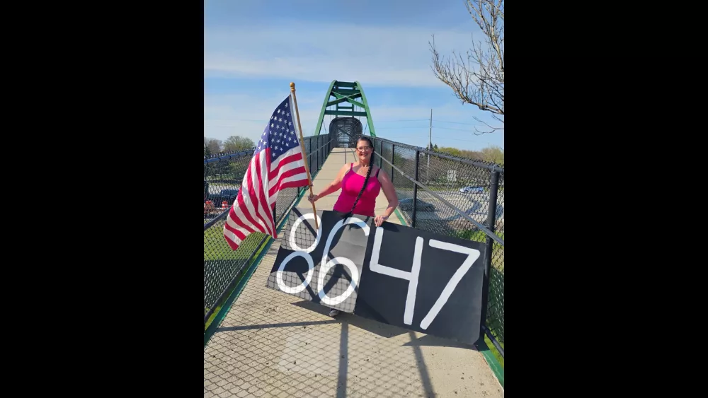 Image of Wendy Hoff holding an American flag with an "8647" banner on the I-94 pedestrian bridge in Fargo