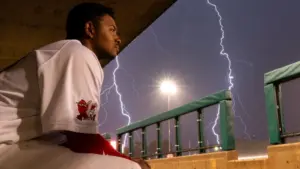 Player sitting on dugout bench with lightning in the background