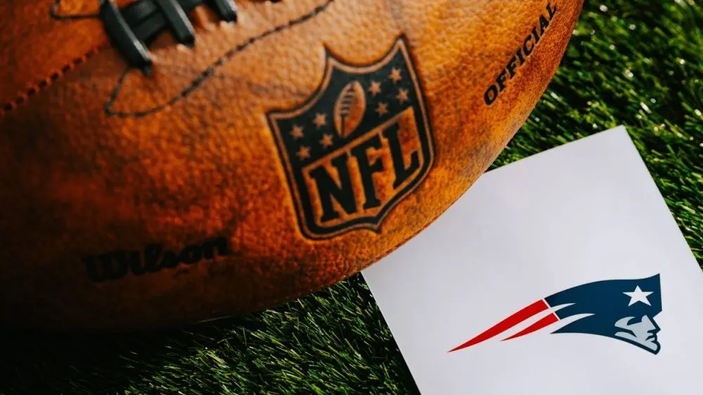 New England Patriots NFL team Logo and American football ball on Green Grass.