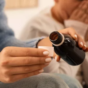 Mother giving cough syrup to her sick son in bed