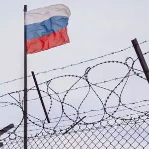 View of russian flag behind barbed wire against cloudy sky. Concept anti-Russian sanctions. A border post on the border of Russia.