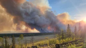 Thick smoke from a Canadian wildfire rises over a forested landscape as the sun sets in the background.