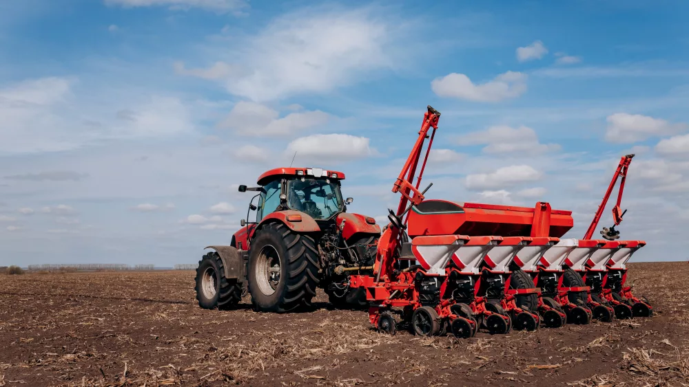 spring-sowing-season-farmer-with-a-tractor-sows-corn-seeds-on-his-field-planting-corn-with-trailed-planter-farming-seeding-the-concept-of-agriculture-and-agricultural-machinery