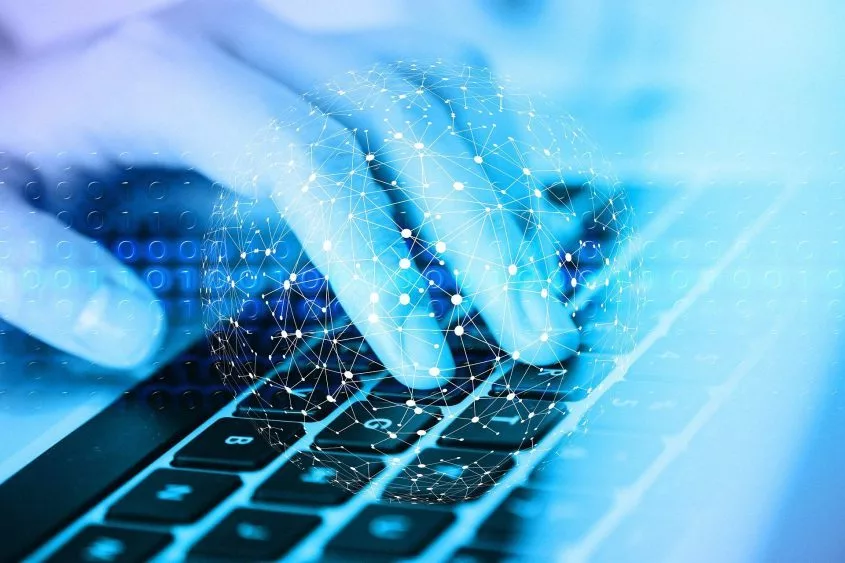 A close-up of a person's hands typing on a keyboard^ with a digital network and binary code overlaid in a blue-toned design^ symbolizing technology and data transmission.