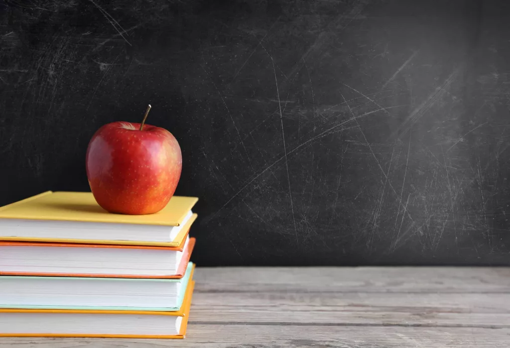 books-and-apple-on-wooden-table-against-school-blackboard