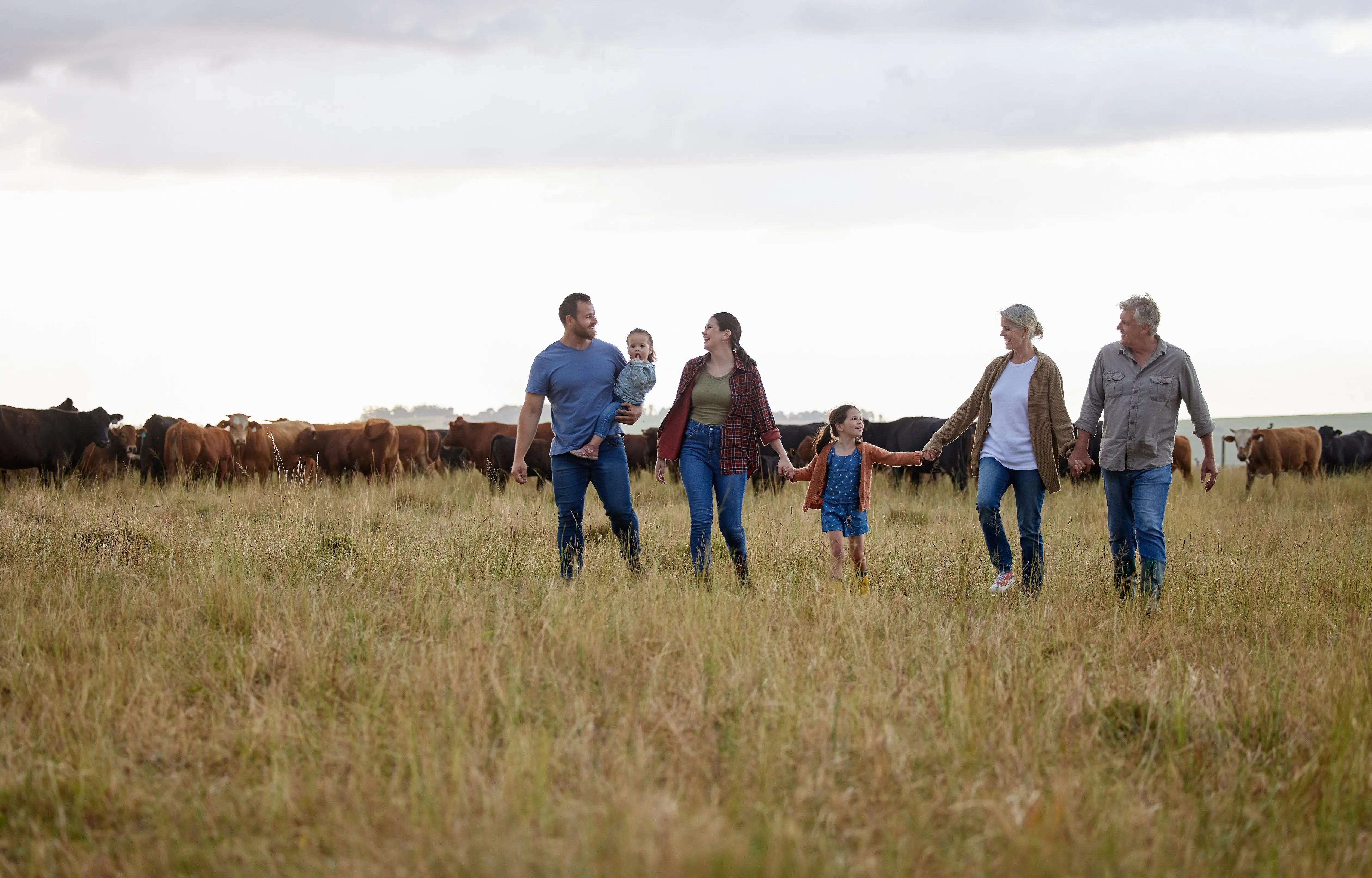 farming-sustainability-and-family-community-on-a-farm-walking-together-with-cows-in-the-background-happy-agriculture-countryside-group-relax-holding-hands-in-a-green-sustainable-field-in-nature