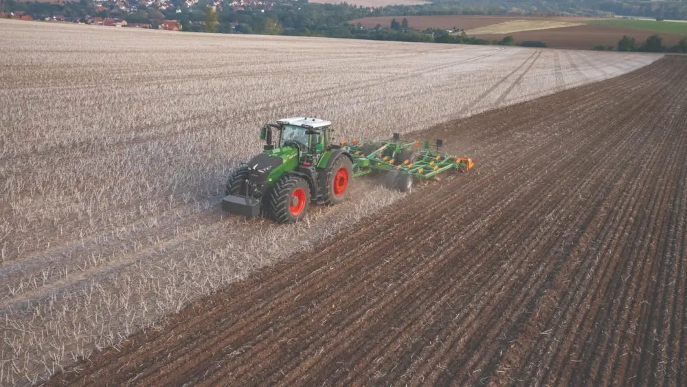 A Fendt tractor with a tillage implement works across a wide harvested field, turning soil in preparation for the next crop.