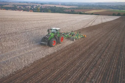 A Fendt tractor with a tillage implement works across a wide harvested field, turning soil in preparation for the next crop.