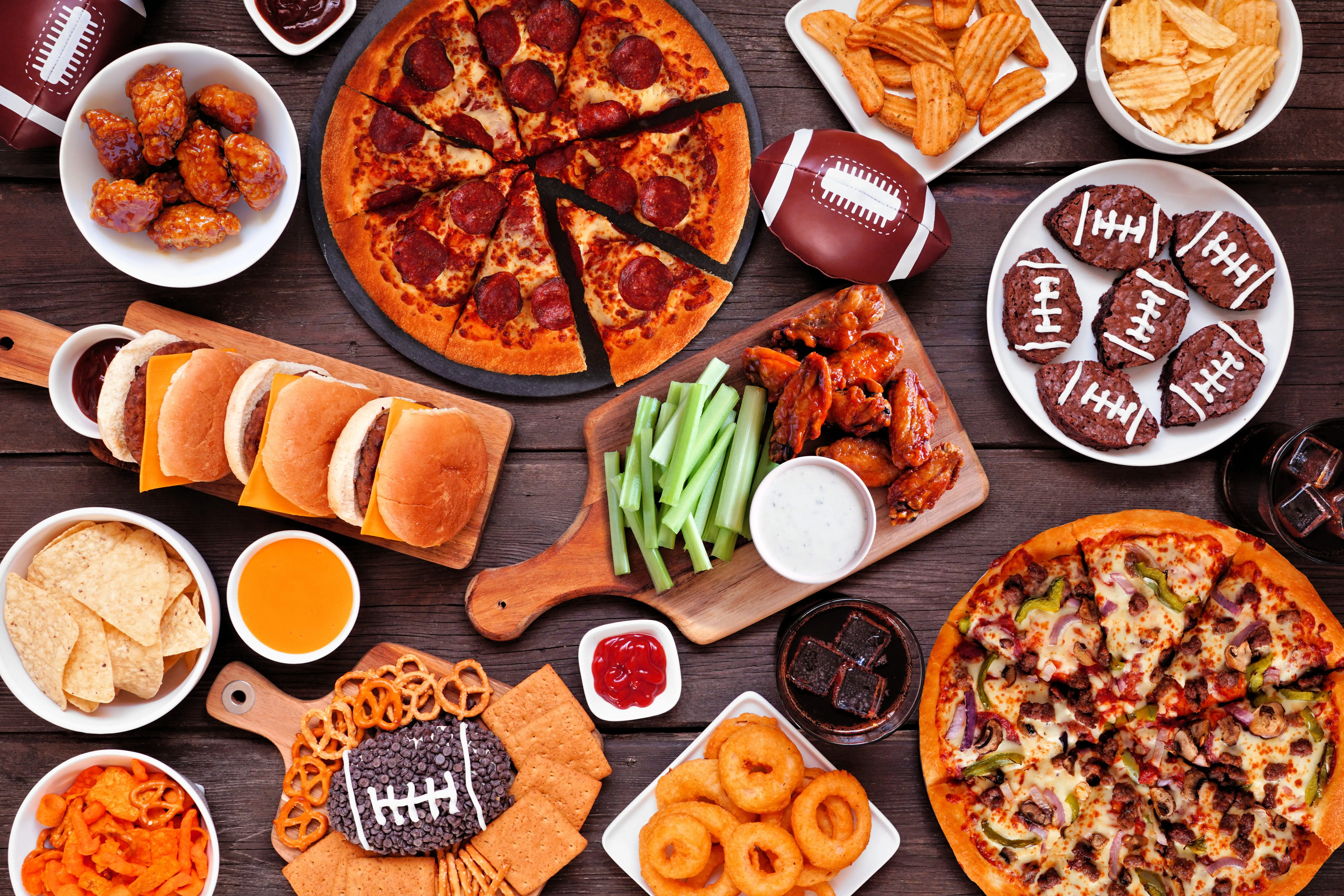 super-bowl-or-football-theme-food-table-scene-pizza-hamburgers-wings-snacks-and-sides-overhead-view-on-a-dark-wood-background