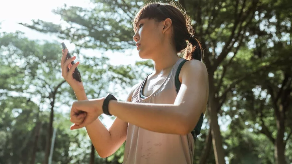 sportswoman with smartphone and fitness bracelet in park (Photo by Ketut Subiyanto)