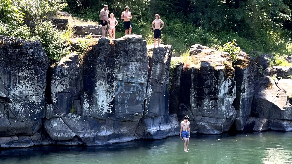 People gather at the top of a high rock outcropping to jump into the Clackamas River in Gladstone, Ore., June 20, 2024. High Rocks Park is a popular spot for cliff jumping and swimming, but it can be dangerous. The air temperature was 88 degrees, while the water temperature on June 20 was 66 degrees - making this ripe for involuntary gasping. That’s why officials implore recreators to use a simple life-saving device – a life jacket.
