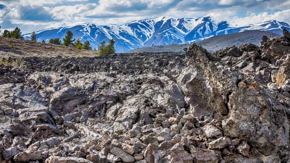 A lava field can be seen with the Pioneer Mountains in the background on April 29, 2024, at Craters of the Moon National Monument and Preserve near Arco. On May 2, 1924, President Calvin Coolidge designated 54,000 acres of volcanic landscape across southern Idaho a national monument, adding that the landscape has “curious and unusual phenomena of great educational value.” (Pat Sutphin for the Idaho Capital Sun)