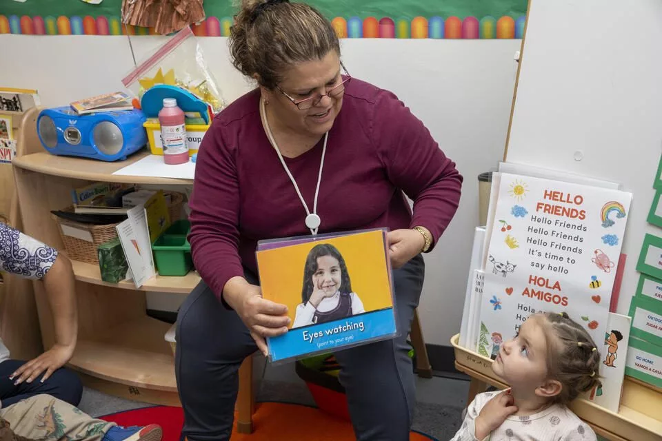 Teacher Maria Saulness, sings with children during circle time at the Sue Krienan Early Learning Center, Skagit/Island Early Head Start Program as Agniia Okara, right, looks on. The Head Start program prioritizes people who come from different backgrounds, offering language support and inclusion for children with disabilities. (Ting-Li Wang for Cascade PBS)