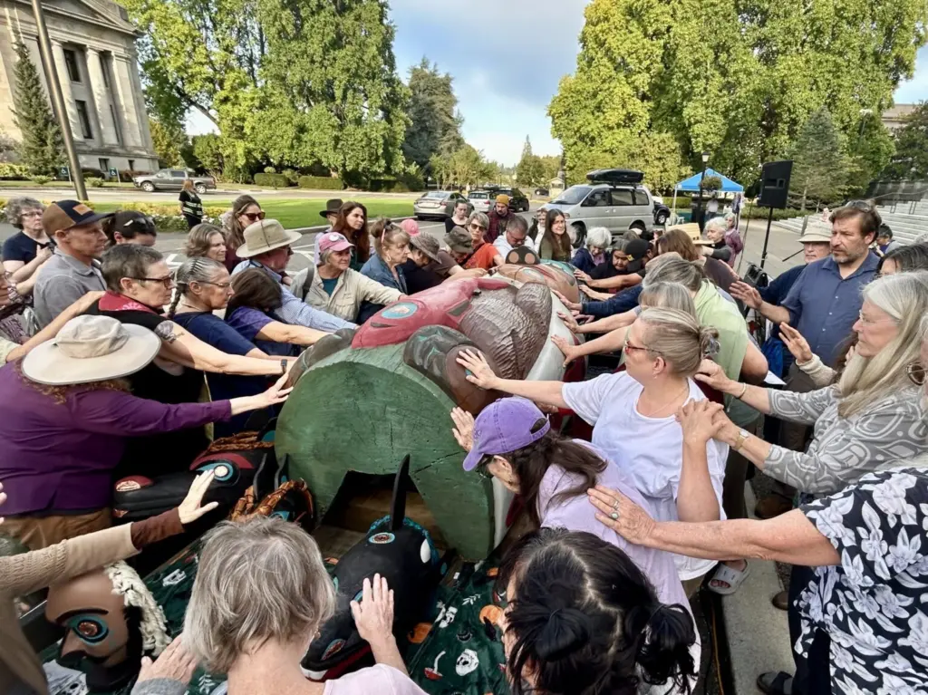 A crowd of about 120 people bless a totem pole and 10 cedar masks carved by the Lummi Nation’s House of Tears outside of the Capitol building in Olympia on Sept. 8, 2025, as part of the Indigenous-led campaign “Xaalh and the Way of the Masks.” The totem and masks will travel 1,700 miles between rally sites in Washington and Oregon before being given to the Lower Elwha Klallam Tribe west of Port Angeles on Sept. 20. (Photo by Emily Fitzgerald/Washington State Standard).