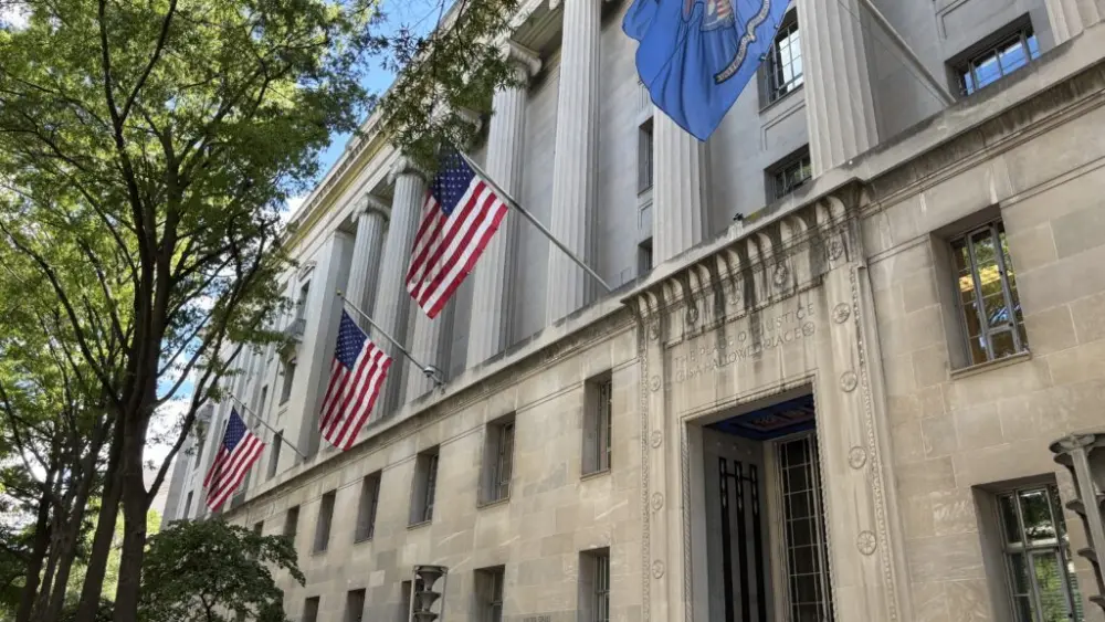 American flags hang alongside the official agency flag at the U.S. Department of Justice building in Washington, D.C., in August. The Justice Department is sharing state voter roll data with the U.S. Department of Homeland Security. (Photo by Jonathan Shorman/Stateline)