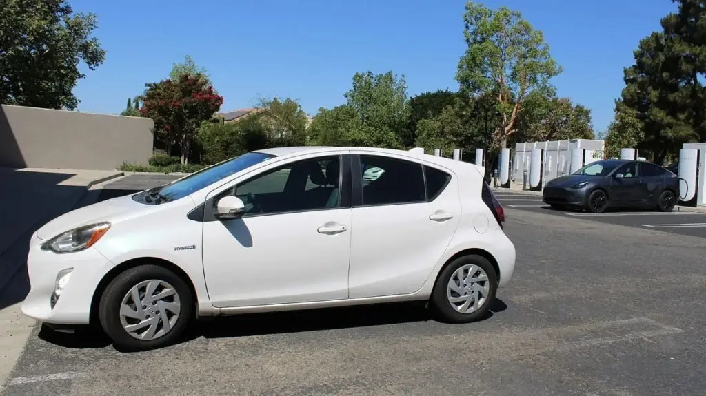 A white Toyota Prius C, a hybrid, is parked near an electric vehicle charging at a Tesla station. Dave Mason / The Center Square