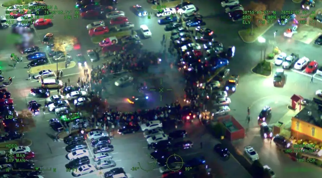 In this image taken from surveillance video, two cars drive in a circle amid a crowd of onlookers in Prince George’s County, Md. Illegal street takeovers, where drivers block roads to perform stunts, have become an increasing concern in cities across the country. (Image via video courtesy of Prince George’s County Police Department)