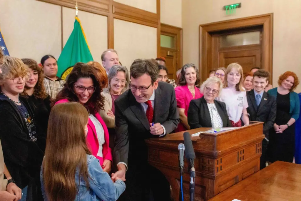 Gov. Bob Ferguson hands over one of the pens he used to sign House Bill 1296, the ‘students bill of rights’ to a child who attended the bill signing. (Photo by Jacquelyn Jimenez Romero/Washington State Standard)