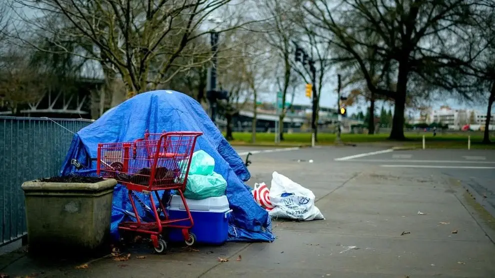 A homeless encampment covered with a blue tarp sits on a city sidewalk with belongings nearby. Photo: Brett Sayle / Pexels