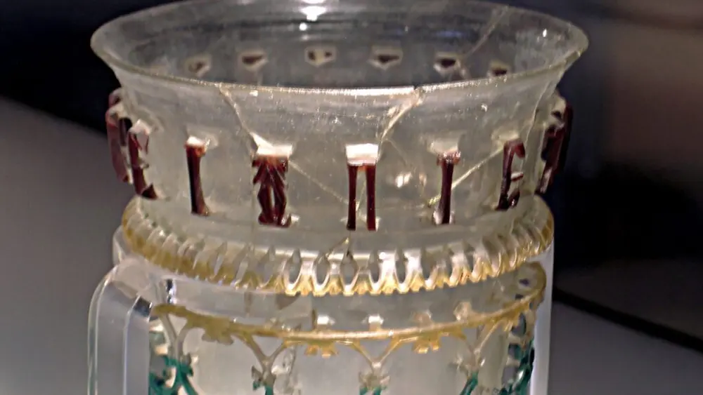 Glass openwork vessel from 300–350 CE with inscription and symbol. Inscription: ΠΙΕ ΖΗCΑΙC ΚΑΛWC ΑΕΙ (Drink, may you live well always!) (photo courtesy of Hallie G. Meredith).