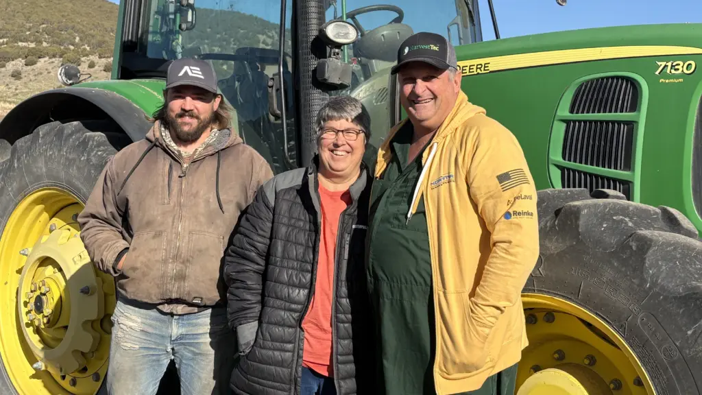 From left, Aaron Larson, Julia Merrill and Glen Merrill pose in front of a tractor at the family’s farm in Swan Lake.