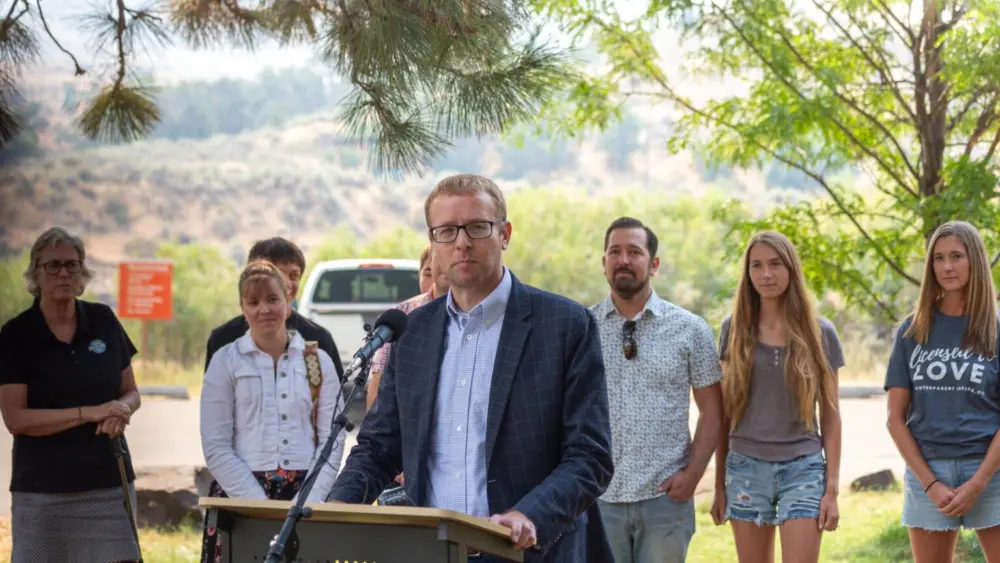 Idaho Department of Health and Welfare Director Alex Adams joins state officials and business leaders to announce the Idaho State Park Foster Family Passport at Lucky Peak State Park, as foster parents and families stand behind him. (Kyle Pfannenstiel/Idaho Capital Sun)