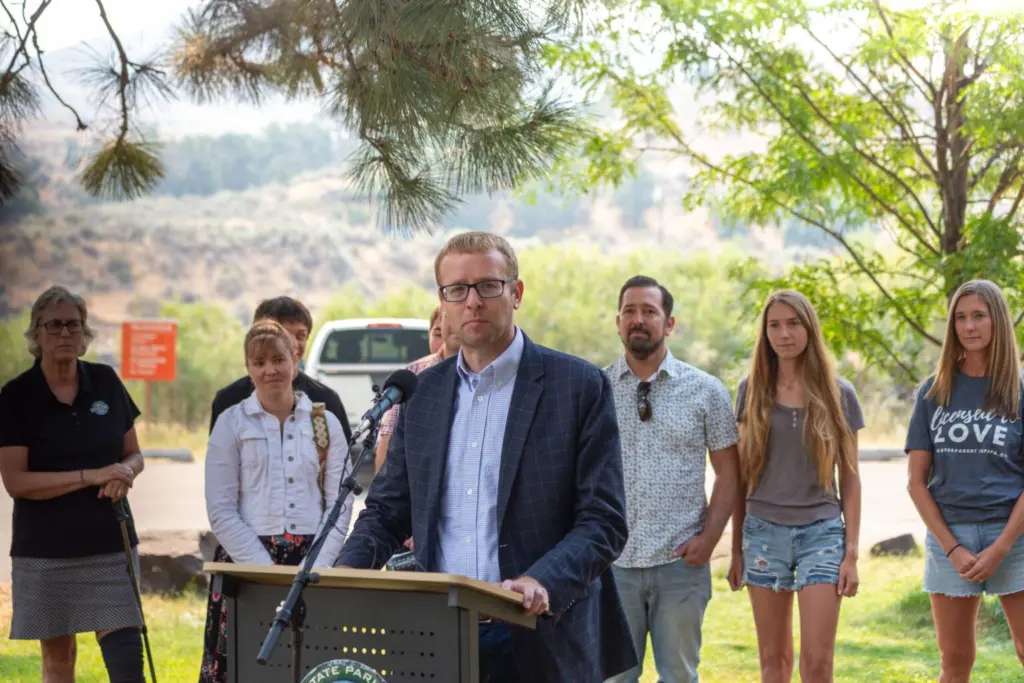 Idaho Department of Health and Welfare Director Alex Adams joins state officials and business leaders to announce the Idaho State Park Foster Family Passport at Lucky Peak State Park, as foster parents and families stand behind him. (Kyle Pfannenstiel/Idaho Capital Sun)