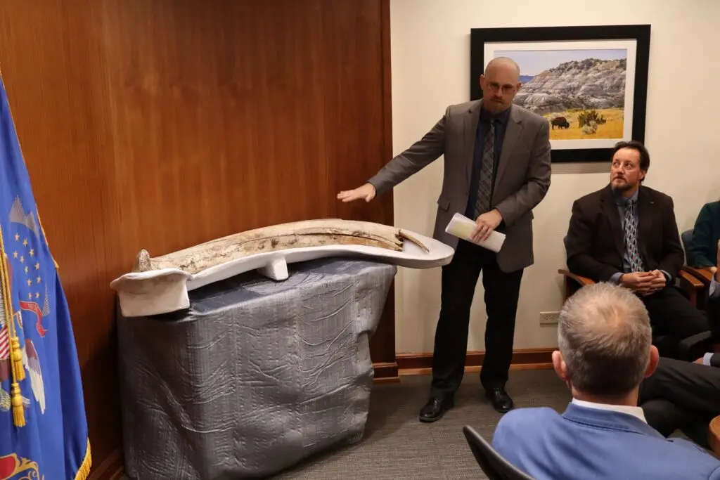 Clint Boyd, North Dakota state paleontologist, shows off a mammoth tusk discovered at a coal mine near Beulah in 2023. He presented the discovery during a Nov. 25, 2025, North Dakota Industrial Commission meeting. (Photo by Jacob Orledge/North Dakota Monitor)