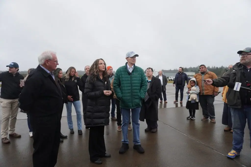 From left to right, Oregon Rep. David Gomberg, D-Otis, Taunette Dixon of the Newport Fishermen’s Wives, and U.S. Sen. Ron Wyden take questions from reporters at the Newport Municipal Airport. (Photo by Shaanth Nanguneri/Oregon Capital Chronicle)