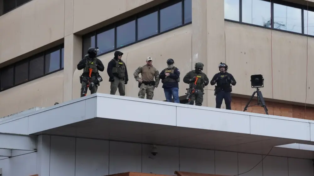 Federal officers with pepper-ball guns look down at protesters at the ICE facility south of downtown Portland on Sunday, Oct. 12, 2025. (Photo by Alex Baumhardt/Oregon Capital Chronicle)