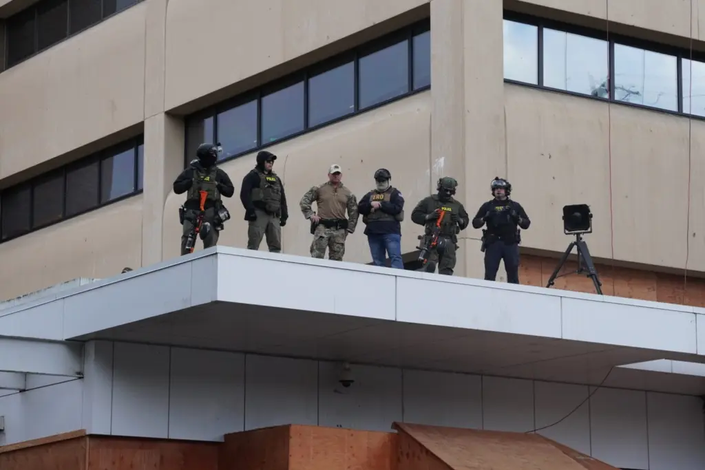 Federal officers with pepper-ball guns look down at protesters at the ICE facility south of downtown Portland on Sunday, Oct. 12, 2025. (Photo by Alex Baumhardt/Oregon Capital Chronicle)