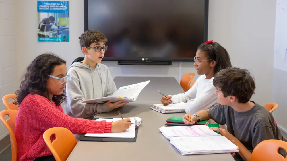 Four middle school students collaborate at a classroom table, participating in a group discussion and taking notes. Photo: Allison Shelley / EDUimages / CC BY-NC 4.0 / Cropped from Original