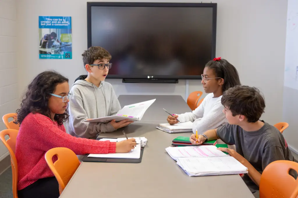 Four middle school students collaborate at a classroom table, participating in a group discussion and taking notes. Photo: Allison Shelley / EDUimages / CC BY-NC 4.0 / Cropped from Original