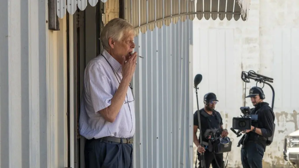 Marion County Record editor-publisher Eric Meyer takes a smoke break Oct. 15, 2025, at his newspaper office after a preliminary hearing for former Marion Police Chief Gideon Cody. A documentary crew films in the distance. (Photo by Sherman Smith/Kansas Reflector)
