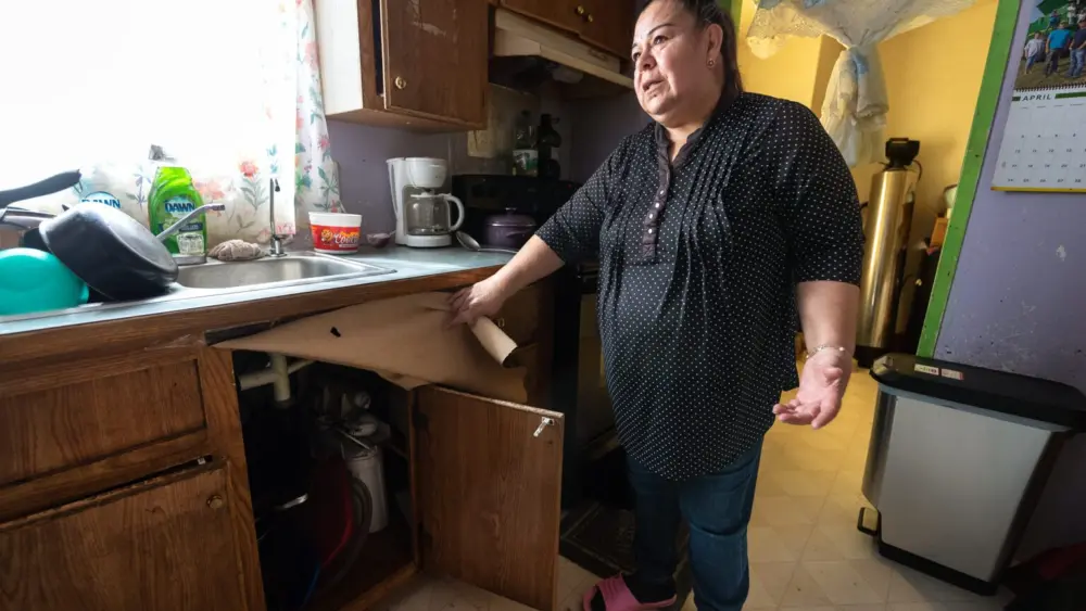 Guadalupe Martinez, of Boardman, says a reverse-osmosis filter installed under the sink that’s meant to reduce the nitrate in her water doesn’t work properly, and the whole-house filter behind her has been broken for years. Her family drinks bottled water to protect themselves from nitrate-tainted groundwater in the Lower Umatilla Basin. (Photo by Kathy Aney/Oregon Capital Chronicle)