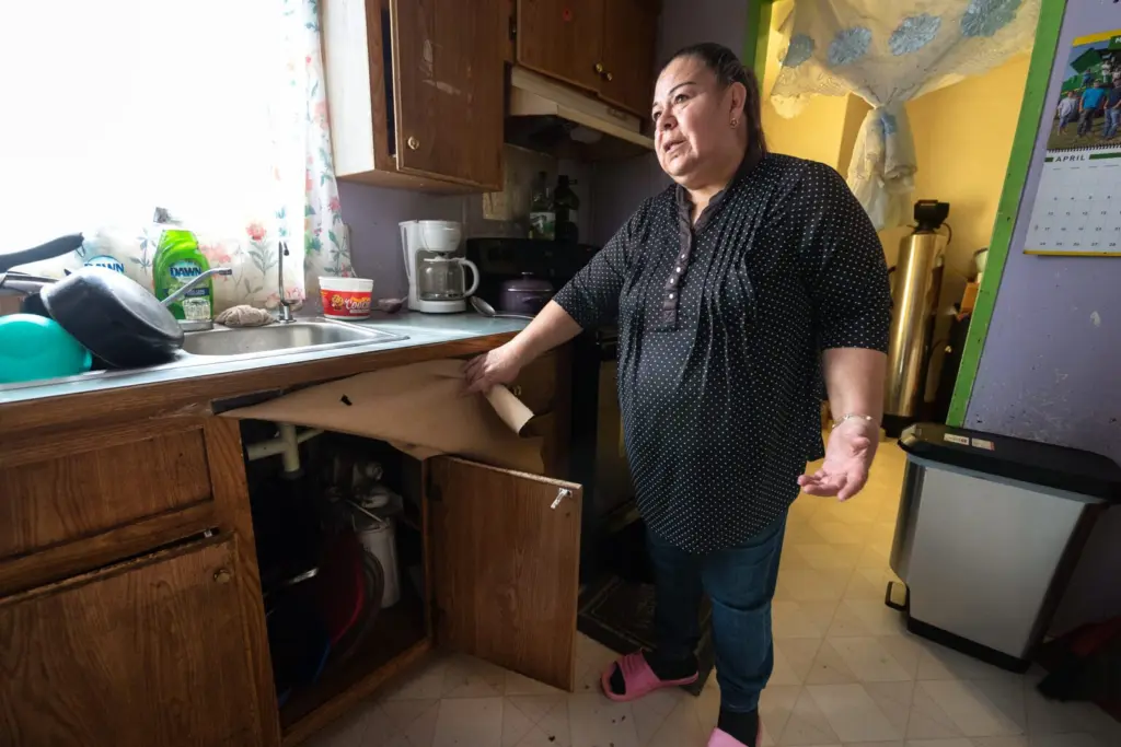 Guadalupe Martinez, of Boardman, says a reverse-osmosis filter installed under the sink that’s meant to reduce the nitrate in her water doesn’t work properly, and the whole-house filter behind her has been broken for years. Her family drinks bottled water to protect themselves from nitrate-tainted groundwater in the Lower Umatilla Basin. (Photo by Kathy Aney/Oregon Capital Chronicle)