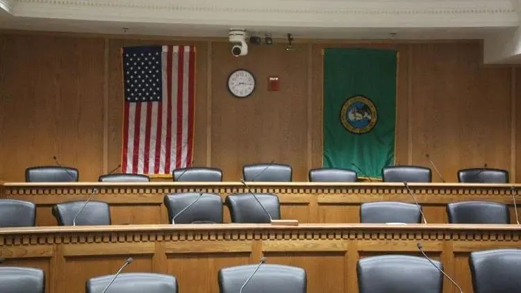 An empty Washington state Senate hearing room inside the Capitol in Olympia, featuring the U.S. and Washington state flags behind the dais. Photo: Tim Clouser / The Center Square