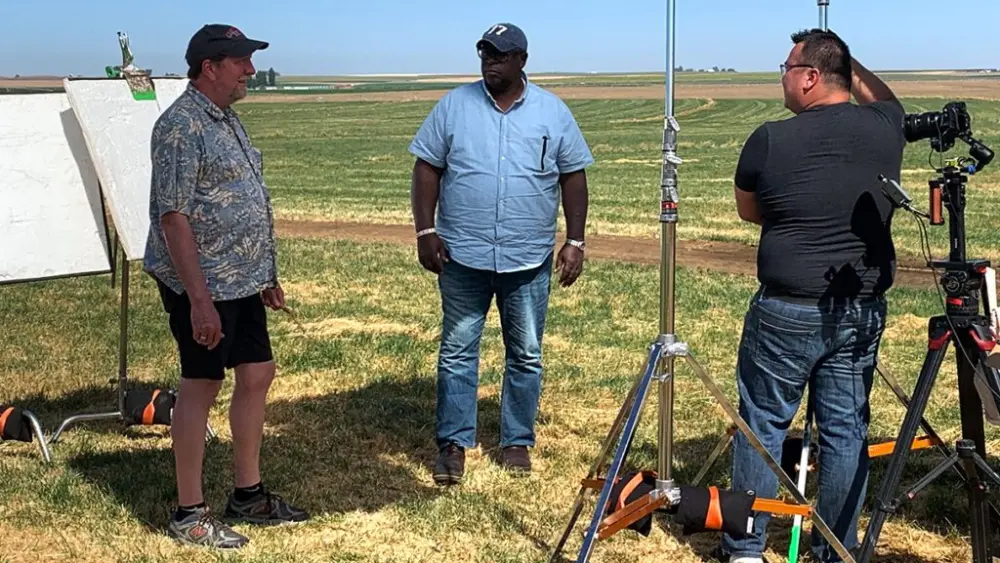 Michael Neff, WSU turfgrass professor, talks with “Ask This Old House” co‑host Lee Gilliam during filming at a grass seed field in Washington, as the PBS crew records a segment on grass seed production and farming in the Pacific Northwest (photo courtesy of Paula Lundt, Seed Program Manager, Washington State Department of Agriculture).