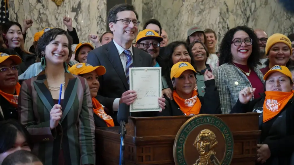 Governor Bob Ferguson appears with supporters of the bill after signing the legislation into law on March 9, 2026. House Bill 2355 establishes labor rights for nannies, gardeners and other domestic workers. (Aspen Ford/Washington State Standard)