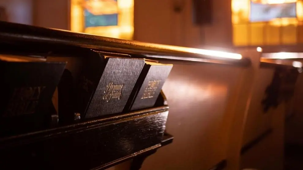 Bibles and hymnals rest in the back of a church pew. Photo: Aaron Burden / Unsplash.