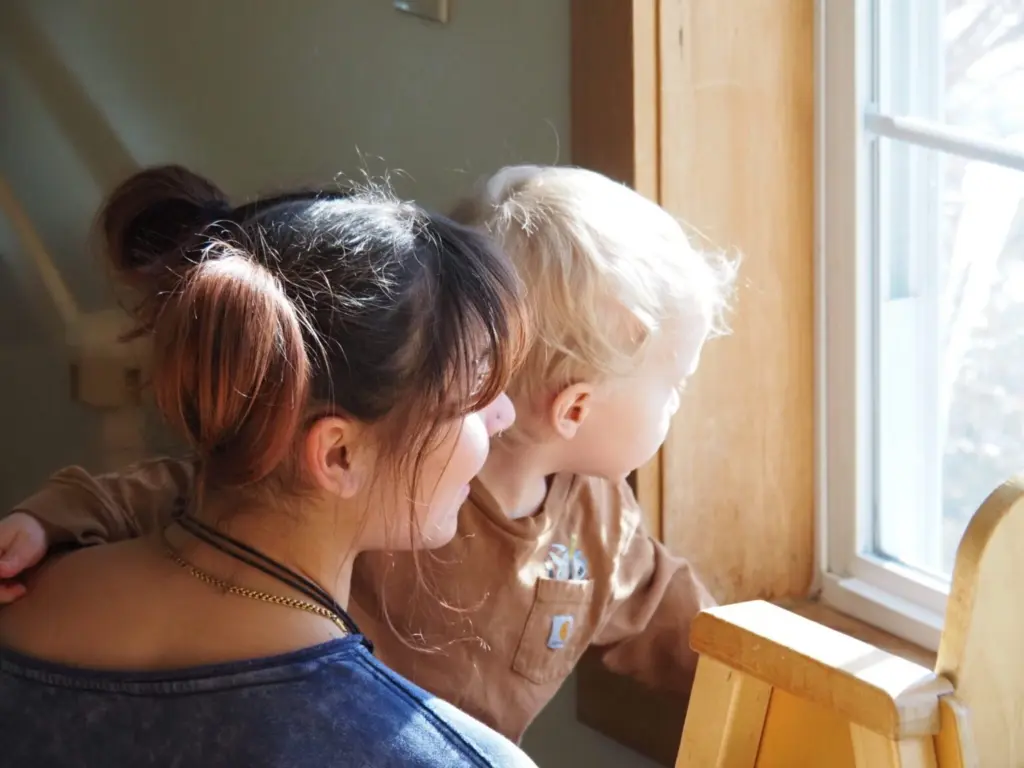 A child care provider and toddler look out the window at Rise for Baby and Family in Keene, N.H. A new analysis of federal data found the gender pay gap between women and men widened last year. (Photo by Maya Mitchell/New Hampshire Bulletin)