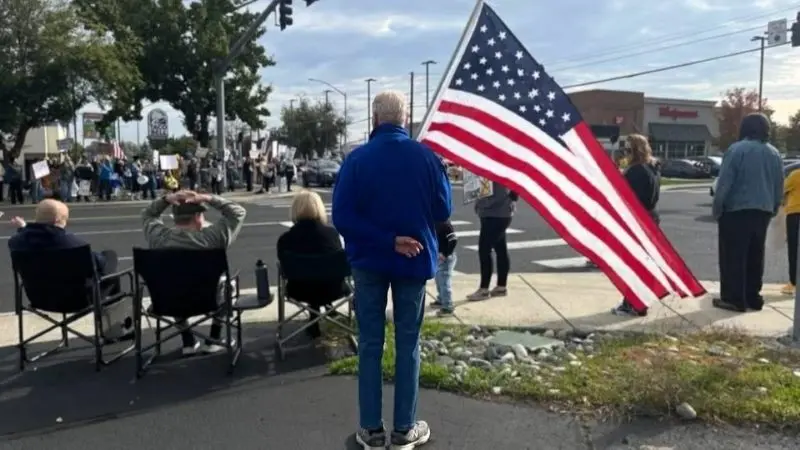People gather near the intersection of 5th and Bridge Streets in Clarkston during a protest on October 18, 2025.