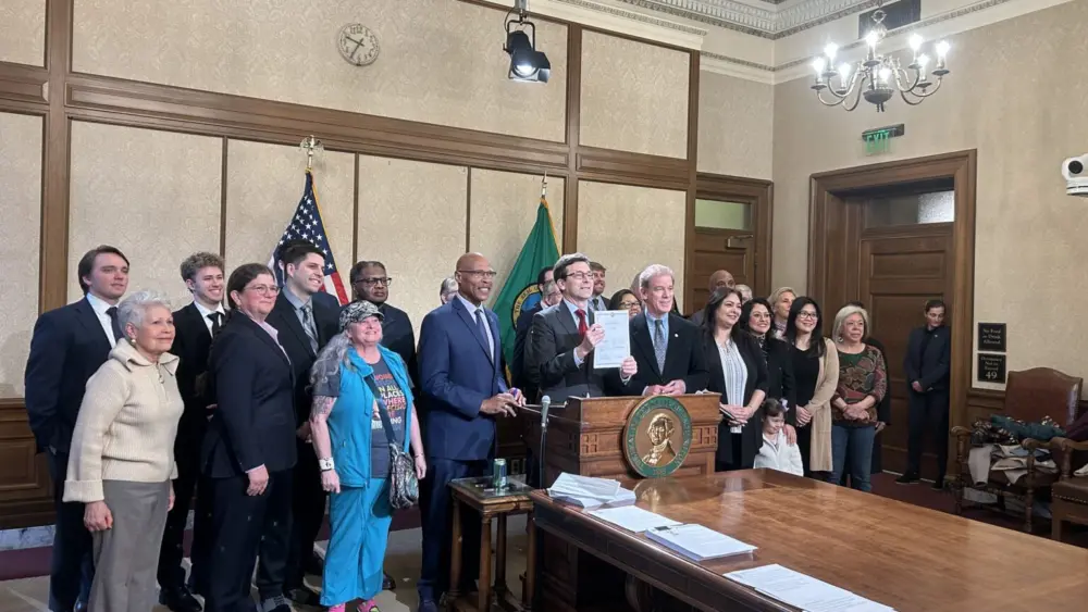 Gov. Bob Ferguson holds up Senate Bill 5974, which sets heightened standards for sheriffs, alongside lawmakers and advocates after signing it on Wednesday, April 1, 2026, in Olympia, Washington. (Photo by Jake Goldstein-Street/Washington State Standard)
