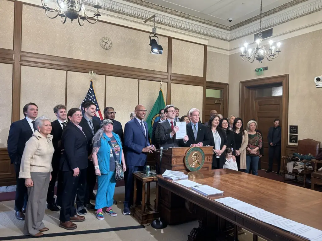 Gov. Bob Ferguson holds up Senate Bill 5974, which sets heightened standards for sheriffs, alongside lawmakers and advocates after signing it on Wednesday, April 1, 2026, in Olympia, Washington. (Photo by Jake Goldstein-Street/Washington State Standard)