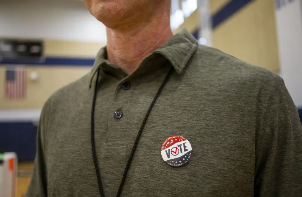 A poll worker proudly displays his vote button while working the general election on Nov. 5, 2024, at North Junior High in Boise. (Pat Sutphin for the Idaho Capital Sun)