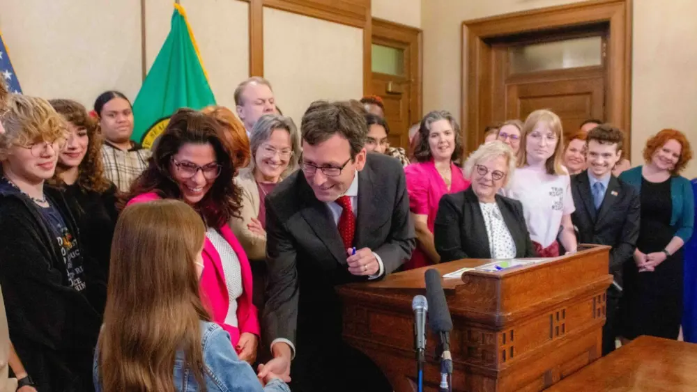 Gov. Bob Ferguson hands over one of the pens he used to sign House Bill 1296, the ‘students bill of rights’ to a child who attended the bill signing. (Photo by Jacquelyn Jimenez Romero/Washington State Standard)